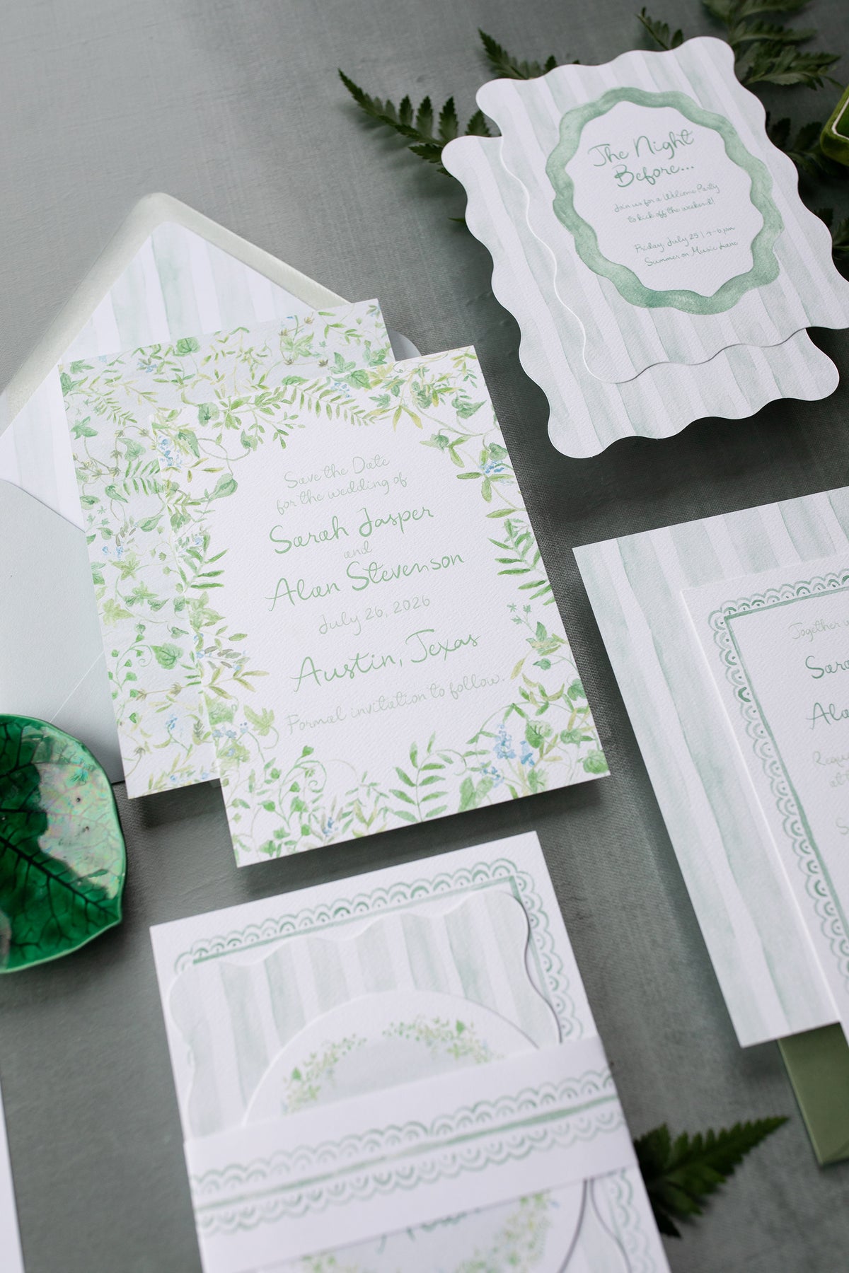 Green and white wedding invitation set with envelopes on a gray surface.