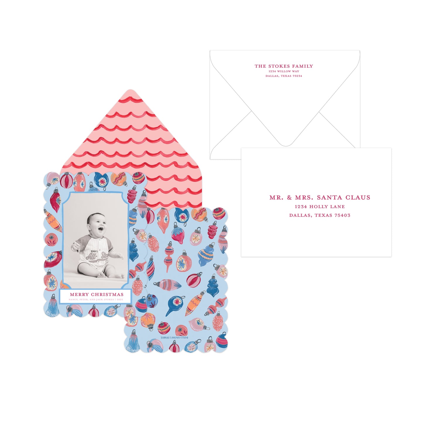 A Christmas-themed invitation card set featuring a scalloped house-shaped card with a baby photo and colorful holiday ornament border, an open pink-and-white scalloped envelope, and a white reply card with red text.