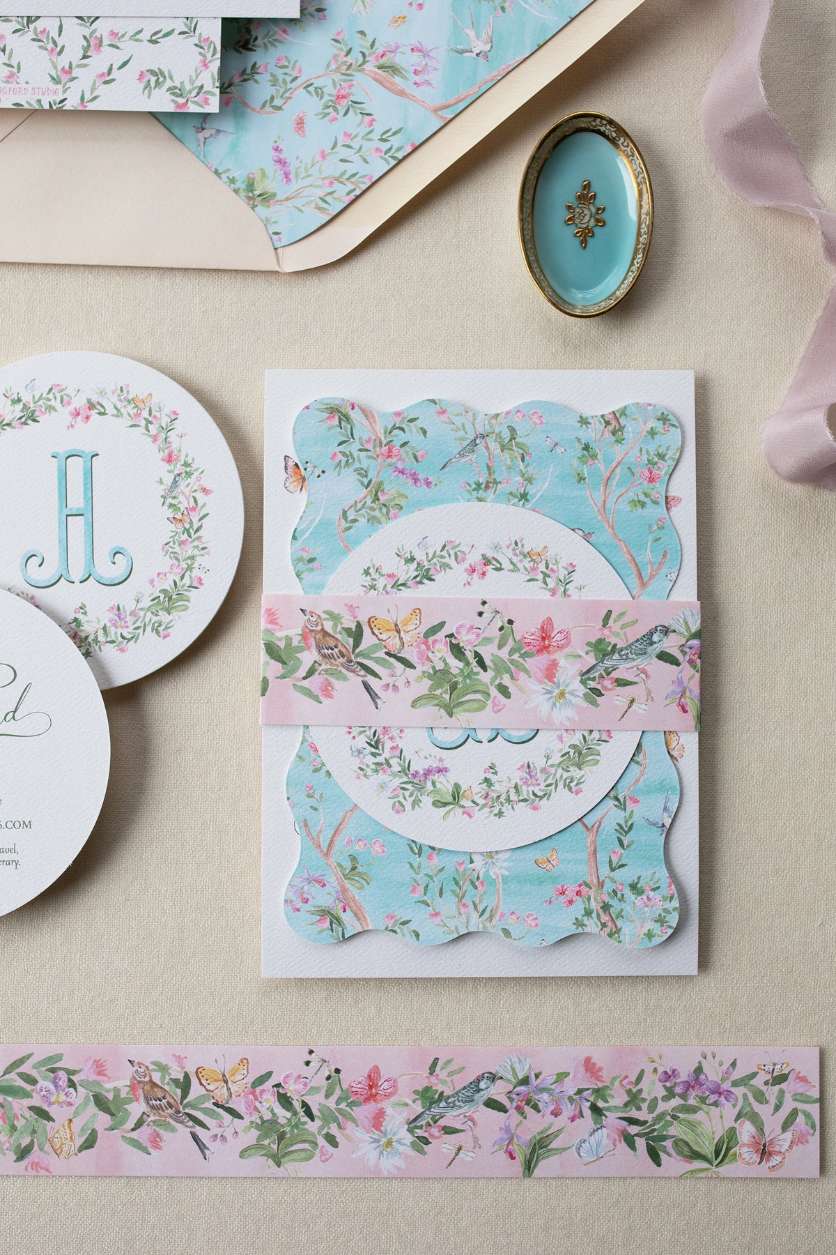 Floral stationery items including a card, envelope, and ribbon on a beige surface.
