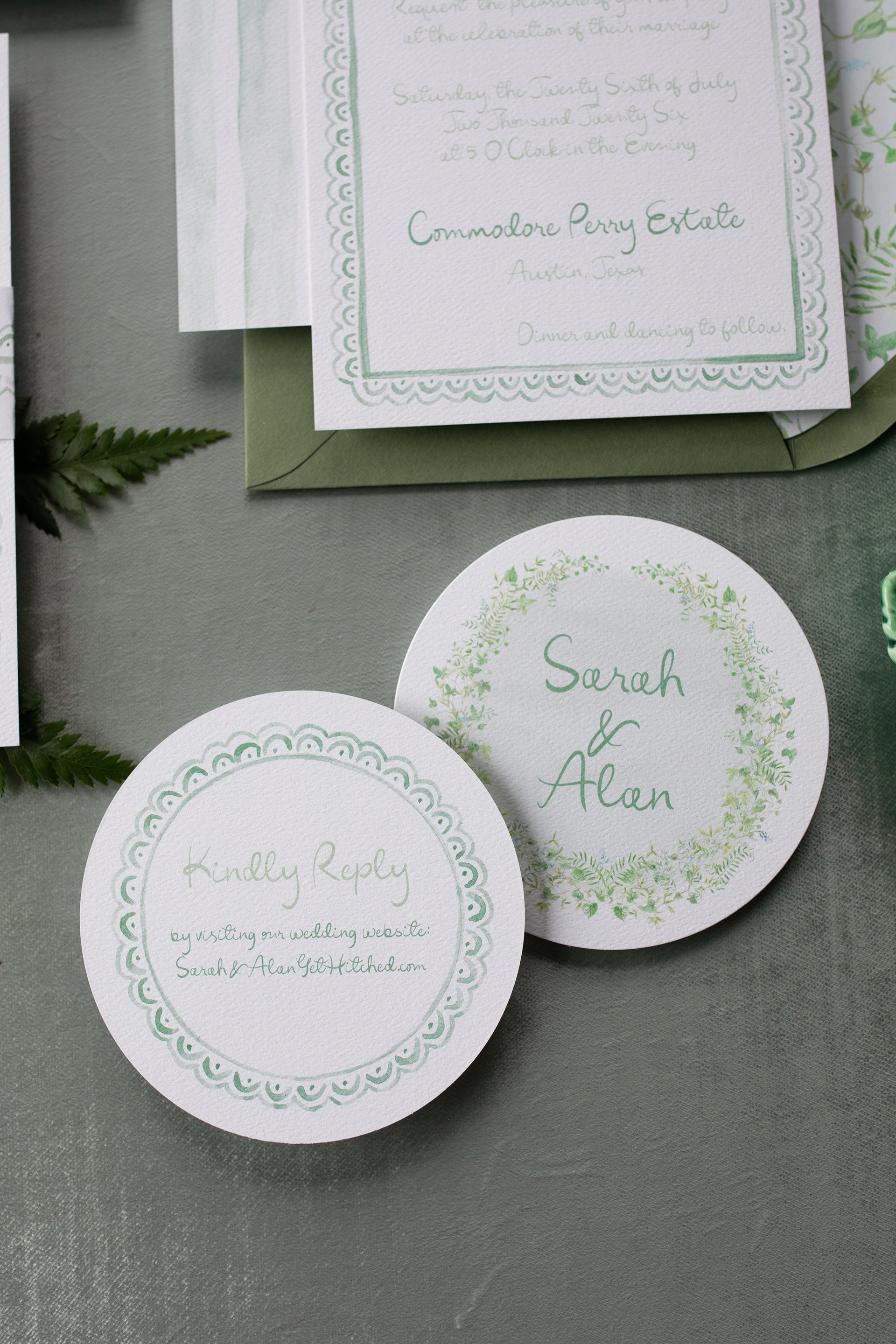 Green and white wedding invitation set with RSVP card on a gray surface.
