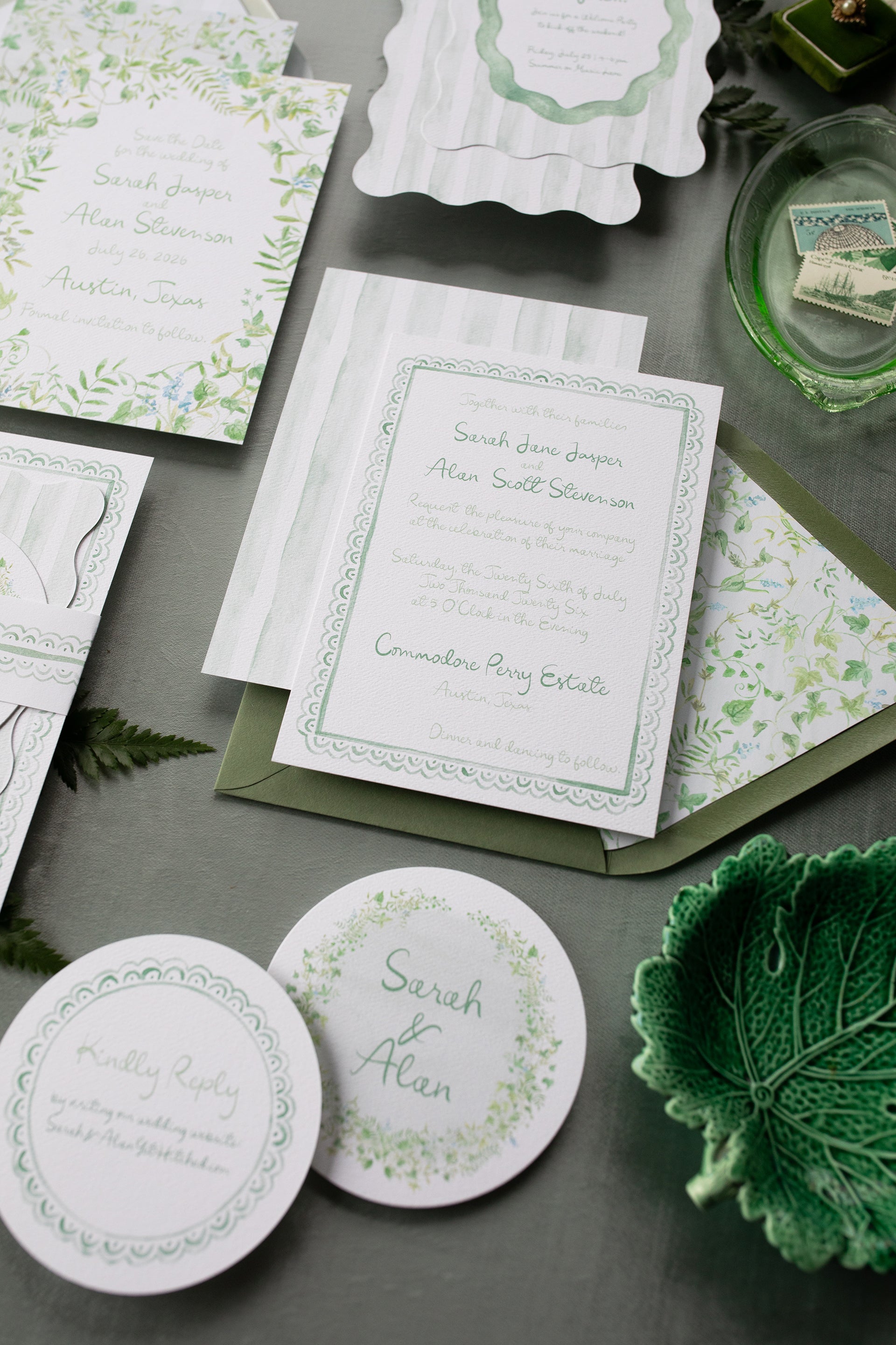Green and white wedding invitations and stationery on a gray surface with green leaves.