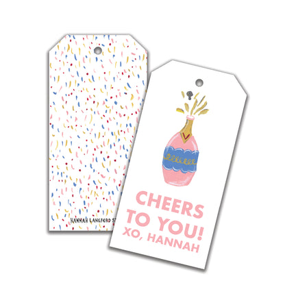 Two customizable gift tags. One with a multicolored dot pattern and the other with a illustrated champagne bottle and text 'CHEERS TO YOU! - XO, HANNAH'.