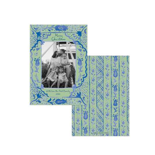 A personalized Christmas photo card set featuring a square front cover and matching envelope. The cards have a light sage green background with blue hand-drawn patterns, including a decorative border around a black-and-white family photo and vertical stripes with pinecone motifs on the envelope.