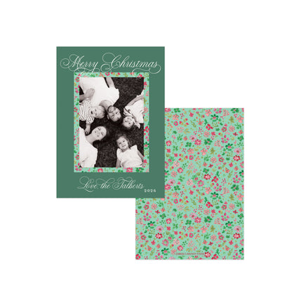 A Christmas photo card set shown on a white background, featuring a dark green front cover with cursive holiday text and a family photo inset, alongside a matching floral-patterned card back in mint green with pink and red berries.