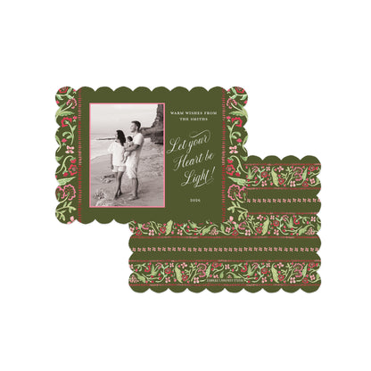 A vintage-style holiday greeting card set with a dark olive green background, scalloped edges, and a red and green floral border. The main card features a black-and-white photo of a couple on a beach.