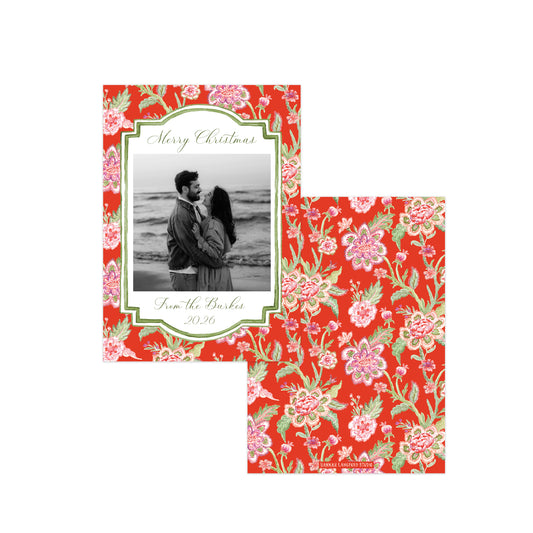 A Christmas-themed photo card and matching envelope set on a white background. The card features a red floral border with pink and green flowers, a central white frame containing a black-and-white couple's photo, and cursive text reading 'Merry Christmas'.