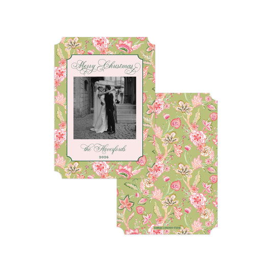 A Christmas greeting card and matching envelope set with a vintage floral pattern in sage green, pink, and white. The front of the card features a central black-and-white photo of a couple embracing under the holiday greeting 'Merry Christmas'.