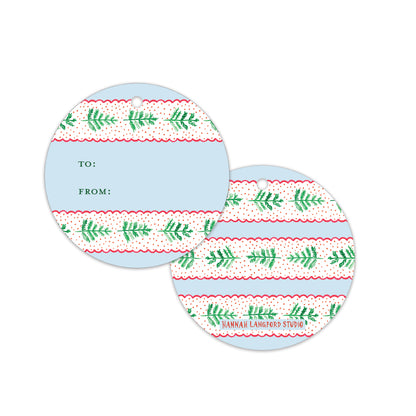 Two round gift tags with a light blue center and a patterned border of green pine branches on a white background with red dotted lines. One tag shows the 'TO:' and 'FROM:' fields.