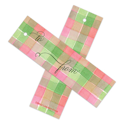 Two rectangular gift tags with a pastel plaid pattern in pink, green, and beige, featuring a white hanging hole and cursive 'to' and 'from' text, shown on a white background.