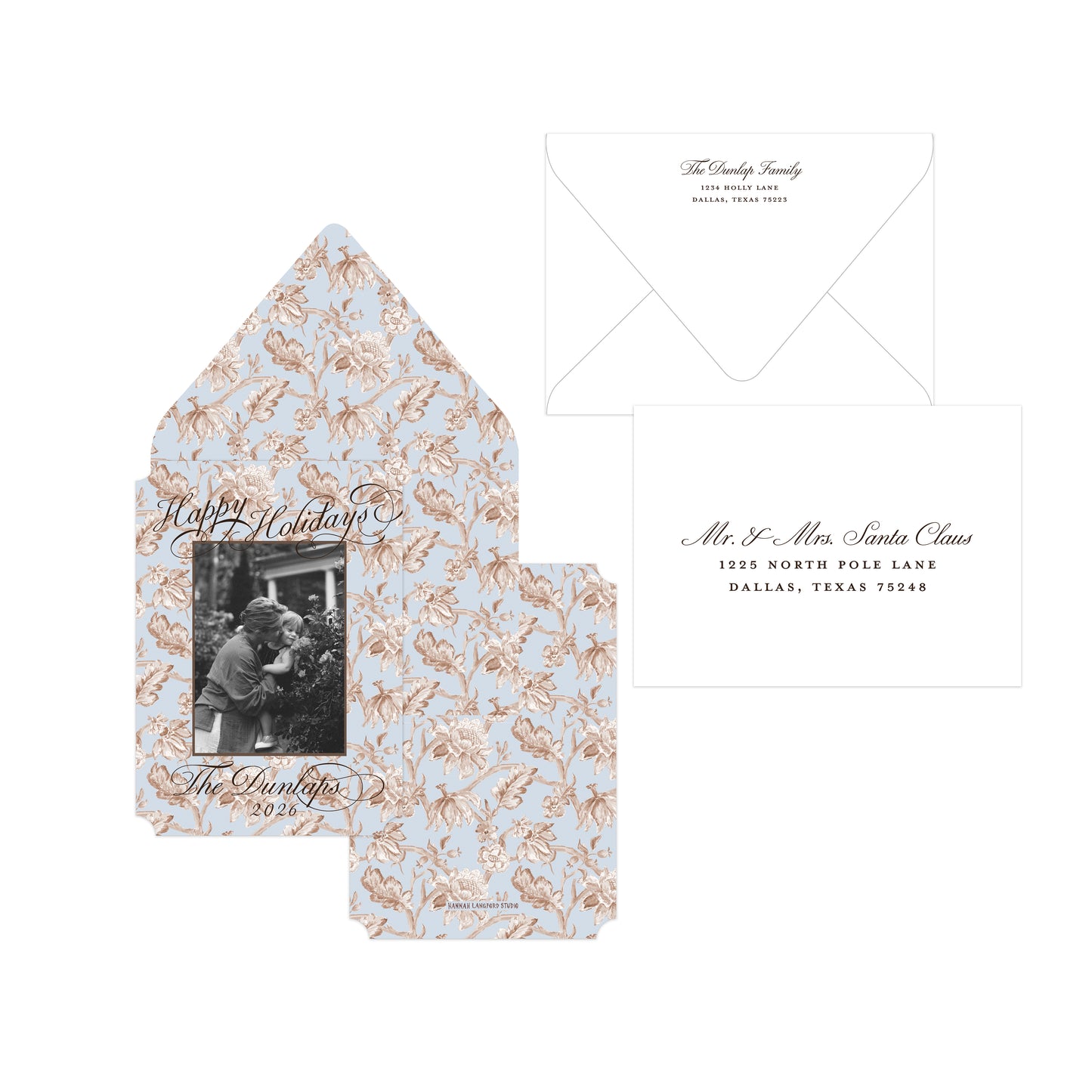 A holiday-themed stationery set featuring a light blue envelope with a rose gold and white holly pattern, a matching inner card with a black-and-white photo insert, and a white address card with elegant script text.
