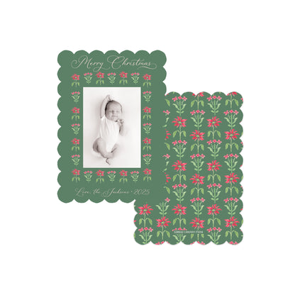 Two personalized Christmas photo cards with scalloped edges on a white background. One card shows a black-and-white baby photo inside a dark green border decorated with pink flowers and green leaves, with 'Merry Christmas' and 'Love, the Johnsons 2025' written at the top and bottom.