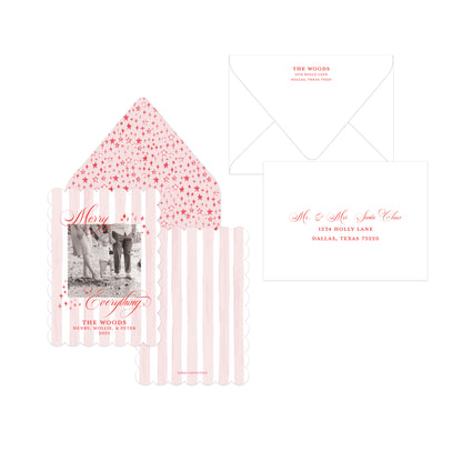 A holiday card collection featuring a scalloped invitation card with a black-and-white photo and pink text, a matching envelope with pink starry pattern, a white envelope, and a white envelope with pink script lettering, all arranged on a white background.