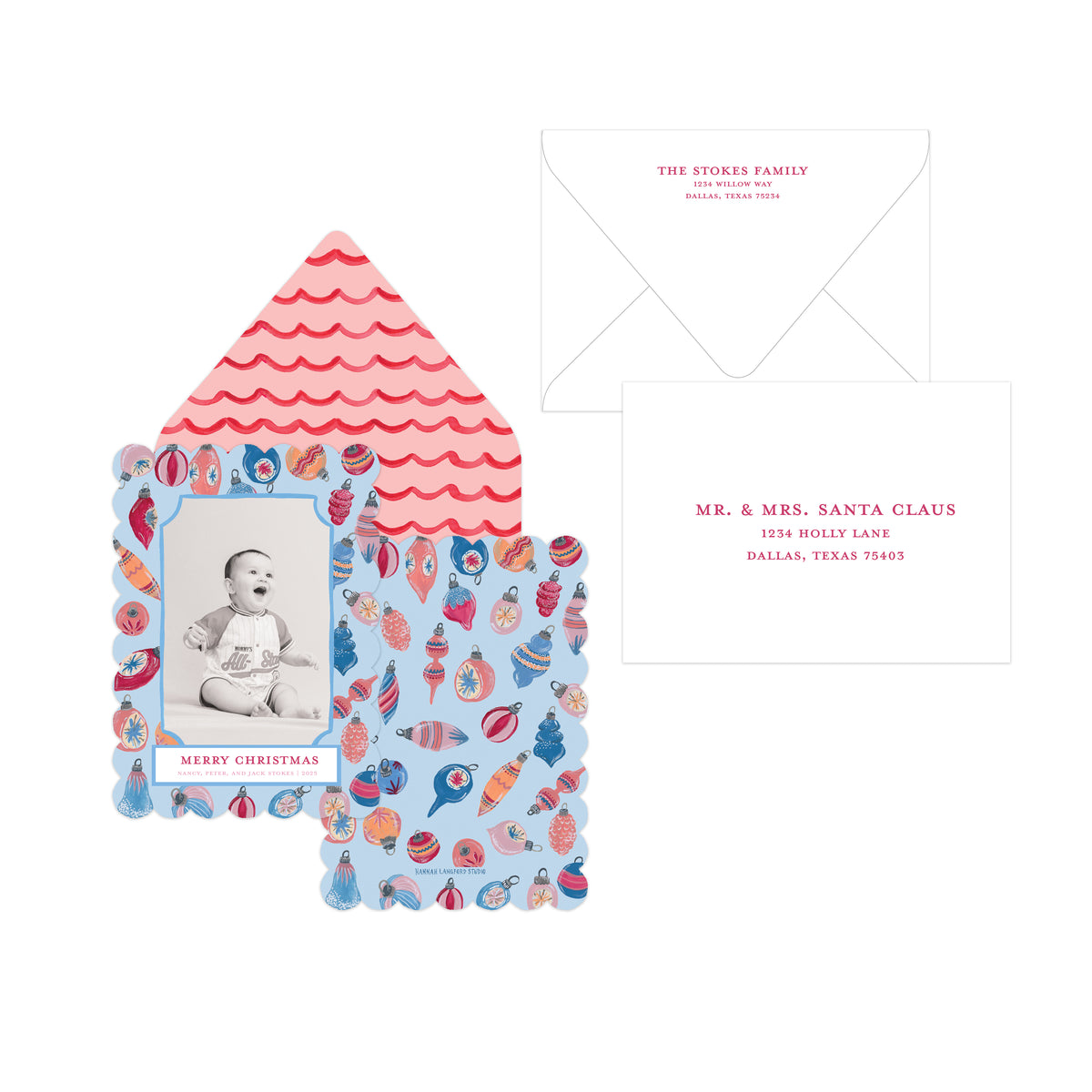 A Christmas-themed invitation card set featuring a scalloped house-shaped card with a baby photo and colorful holiday ornament border, an open pink-and-white scalloped envelope, and a white reply card with red text.