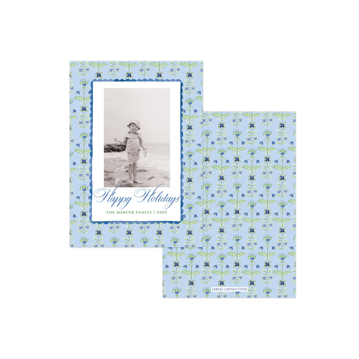 Two personalized holiday photo cards with a light blue background and a repeating green and blue floral pattern. One card shows a black-and-white photo of a child on a beach with the text 'Happy Holidays' and the family name, while the other shows only the patterned design.
