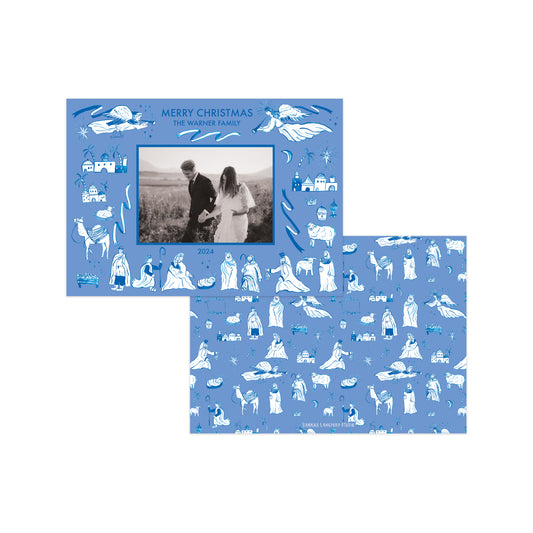 Two blue Christmas-themed photo cards with white line-art illustrations of nativity scenes and animals, shown overlapping on a white background. One card features a central black-and-white photo of a couple, and the other shows a full patterned design.