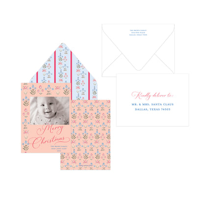 A Christmas personalized card set featuring a peach and blue floral patterned card with a baby photo, matching patterned envelope liner, a white envelope, and a white reply card with pink and blue text.