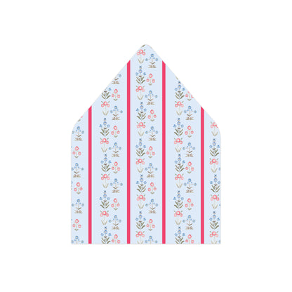 A pointed envelope flap or paper liner with a vertical striped pattern featuring small floral motifs in blue, pink, green, and brown on a white background, flanked by two bright pink stripes.