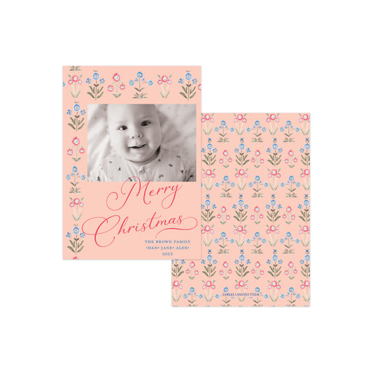 Two personalized Christmas photo cards with a soft peach background and a delicate floral border pattern in pink, blue, and green. One card features a baby's black-and-white photo with 'Merry Christmas' written in pink script, and the other shows the repeating floral pattern.