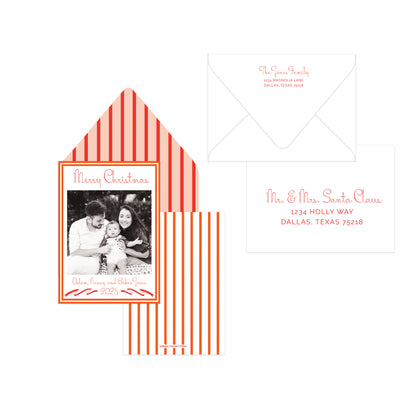 A holiday stationery set on a white background, including a photo card with a red-and-white striped envelope, a white envelope, and a white address label with red script text.