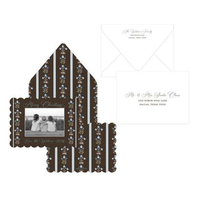 A Christmas-themed invitation suite featuring a dark brown envelope with vertical white stripes and blue floral accents, a matching scalloped photo insert, a white card with elegant script text, and a white envelope on a plain white background.
