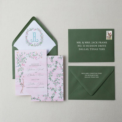 Wedding invitation set with pink card, green envelopes, and floral design on a beige background