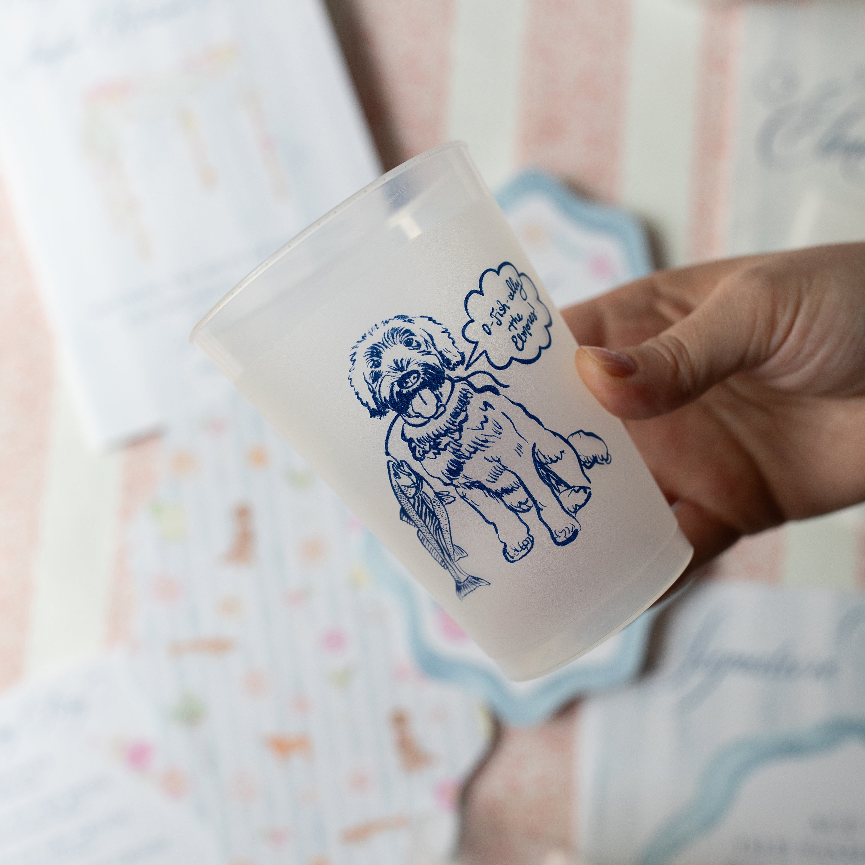 Hand holding a white mug with blue bear illustration and text on a soft, patterned background