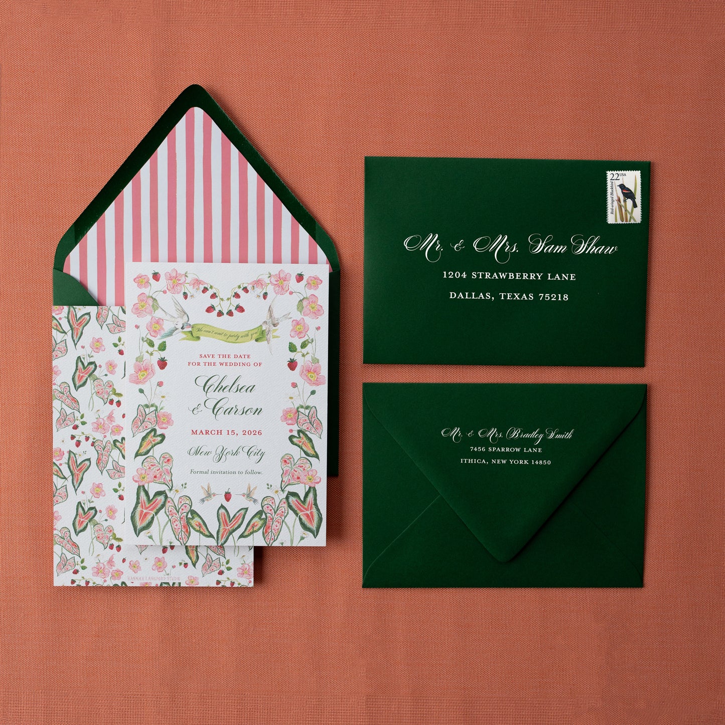 Wedding invitation set with floral design, striped envelope liner, and green envelopes on a red background.