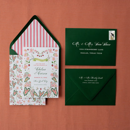 Wedding invitation set with floral design, striped envelope liner, and green envelopes on a red background.