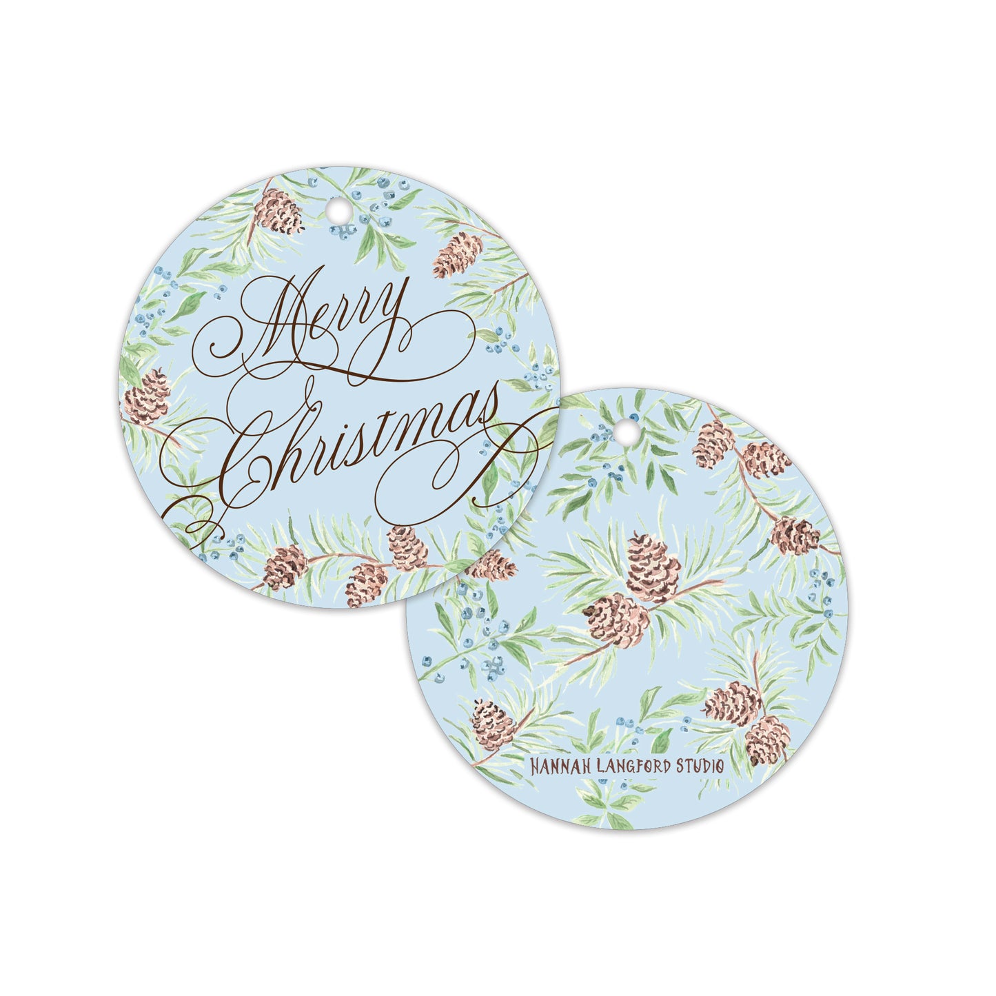 Two round hanging gift tags with a light blue background, decorated with a green pine and berry botanical pattern, brown pinecones, and elegant cursive text reading 'Merry Christmas'.