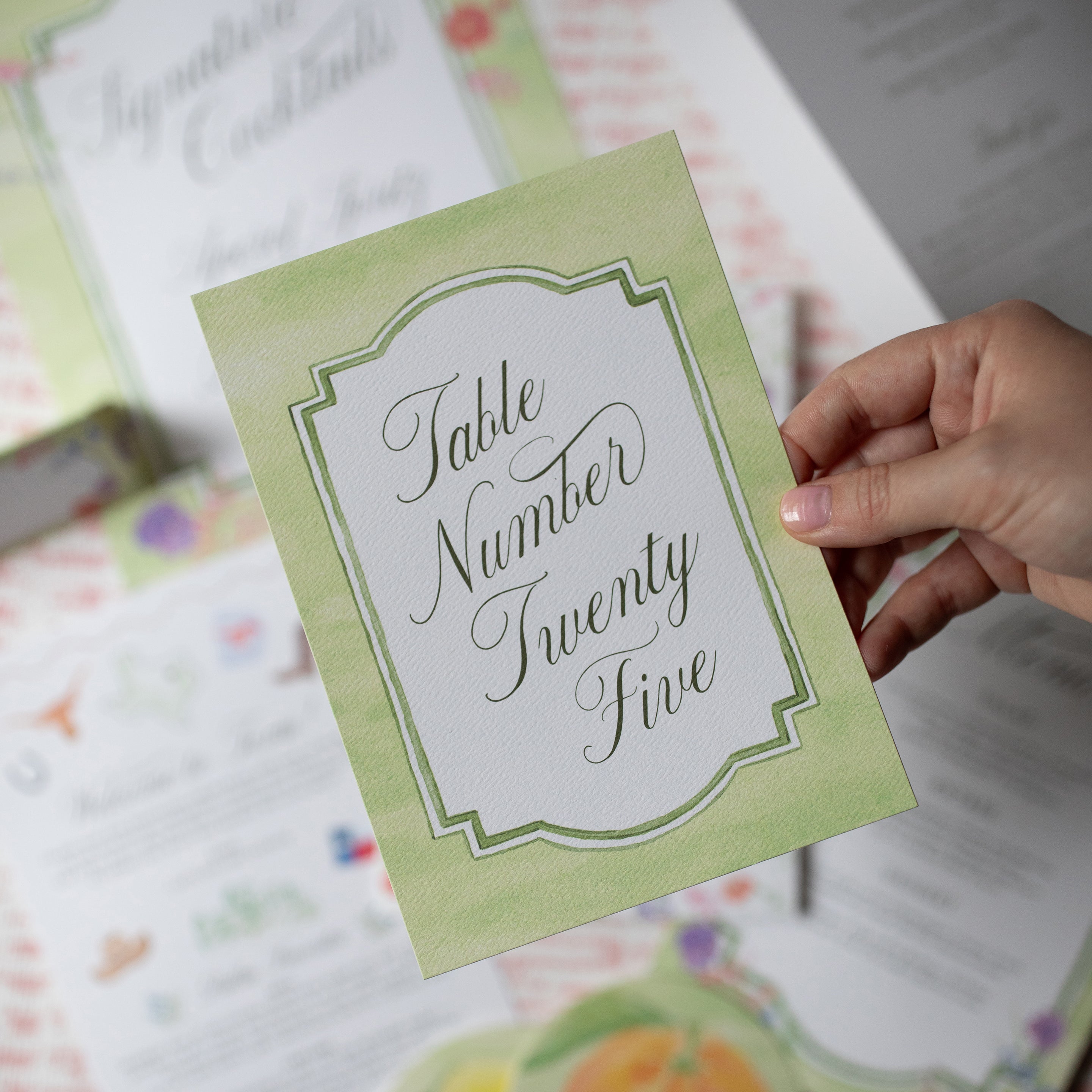 Hand holding a green table number card with 'Table Number Twenty Five' text.
