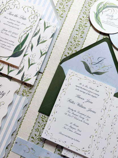 Collection of wedding invitations with greenery and elegant designs on a textured surface.