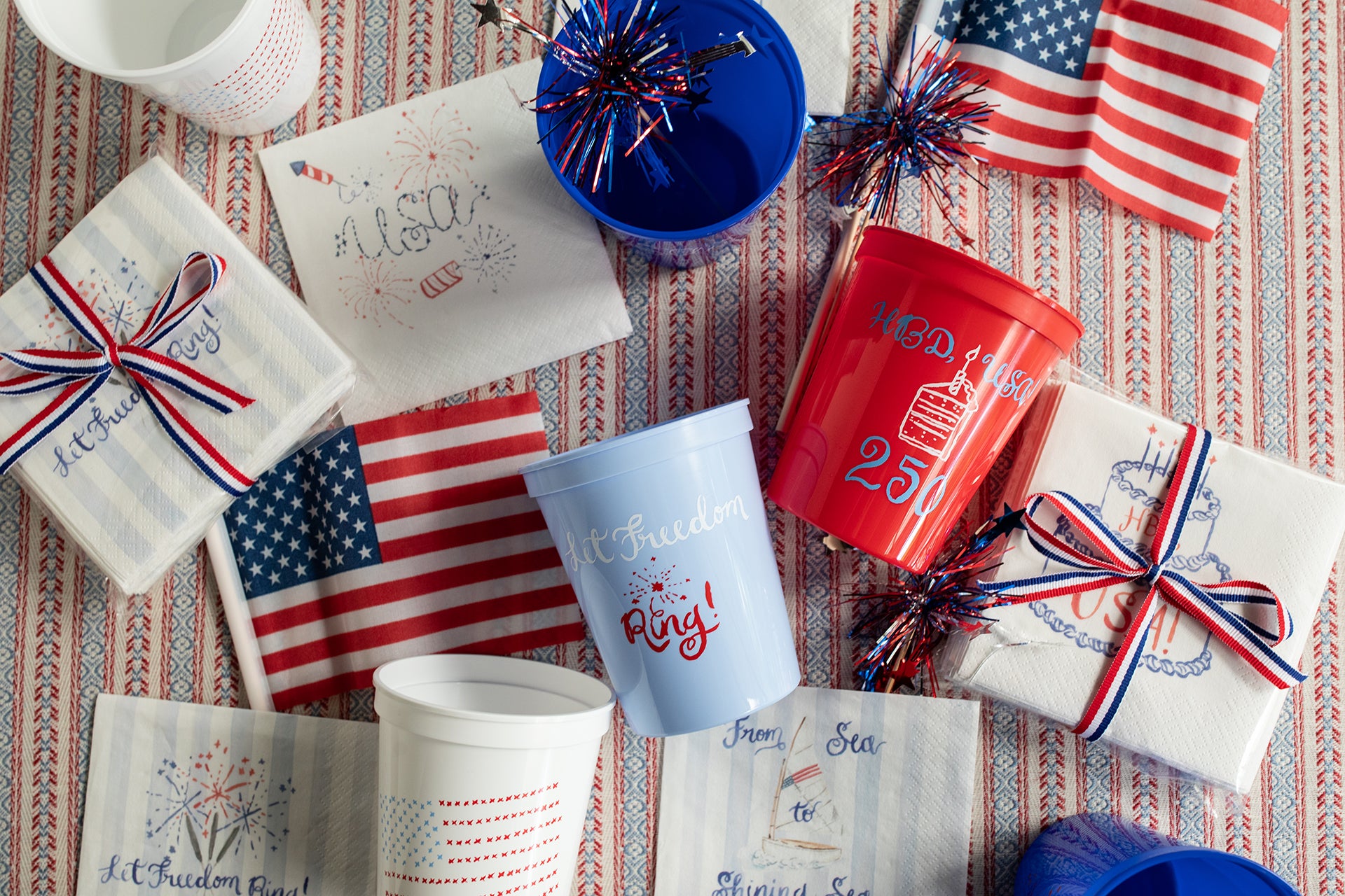 Table setting with American flags, cups, and small packages on a patterned tablecloth.