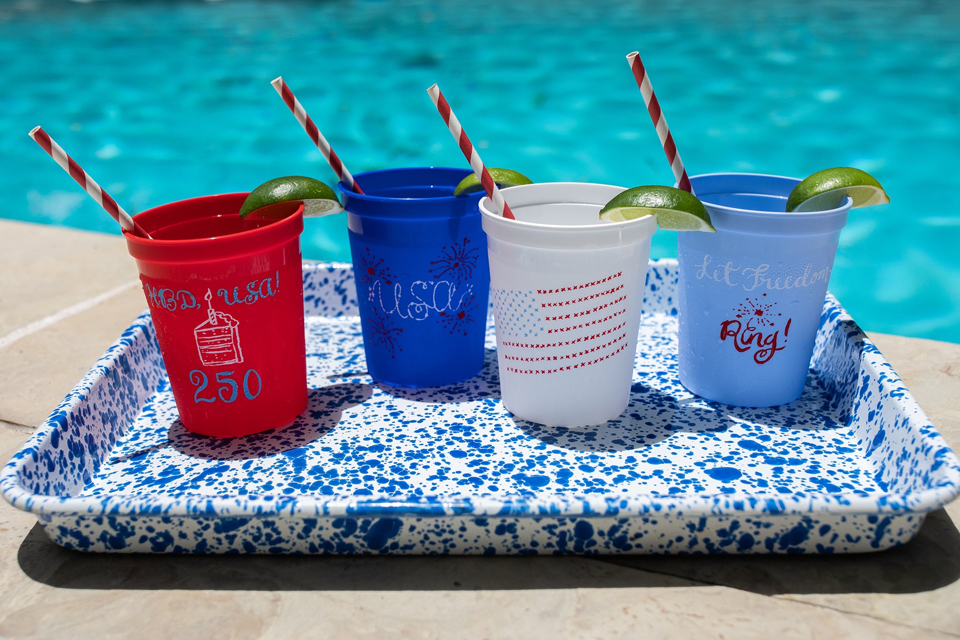 Four cups with straws and pool-themed text on a tray by a pool.