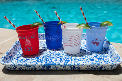 Four cups with straws and pool-themed text on a tray by a pool.