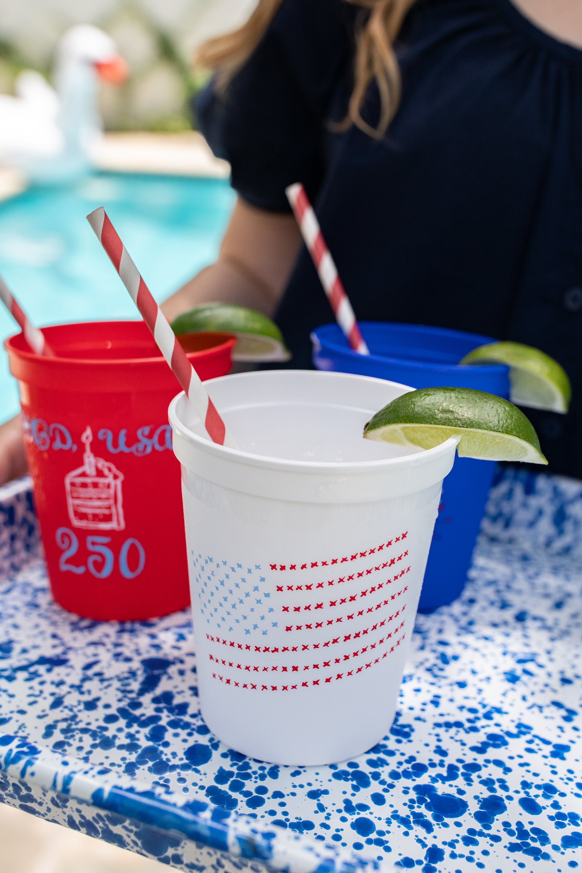 Red and white cups with straws and lime wedges on a poolside table.