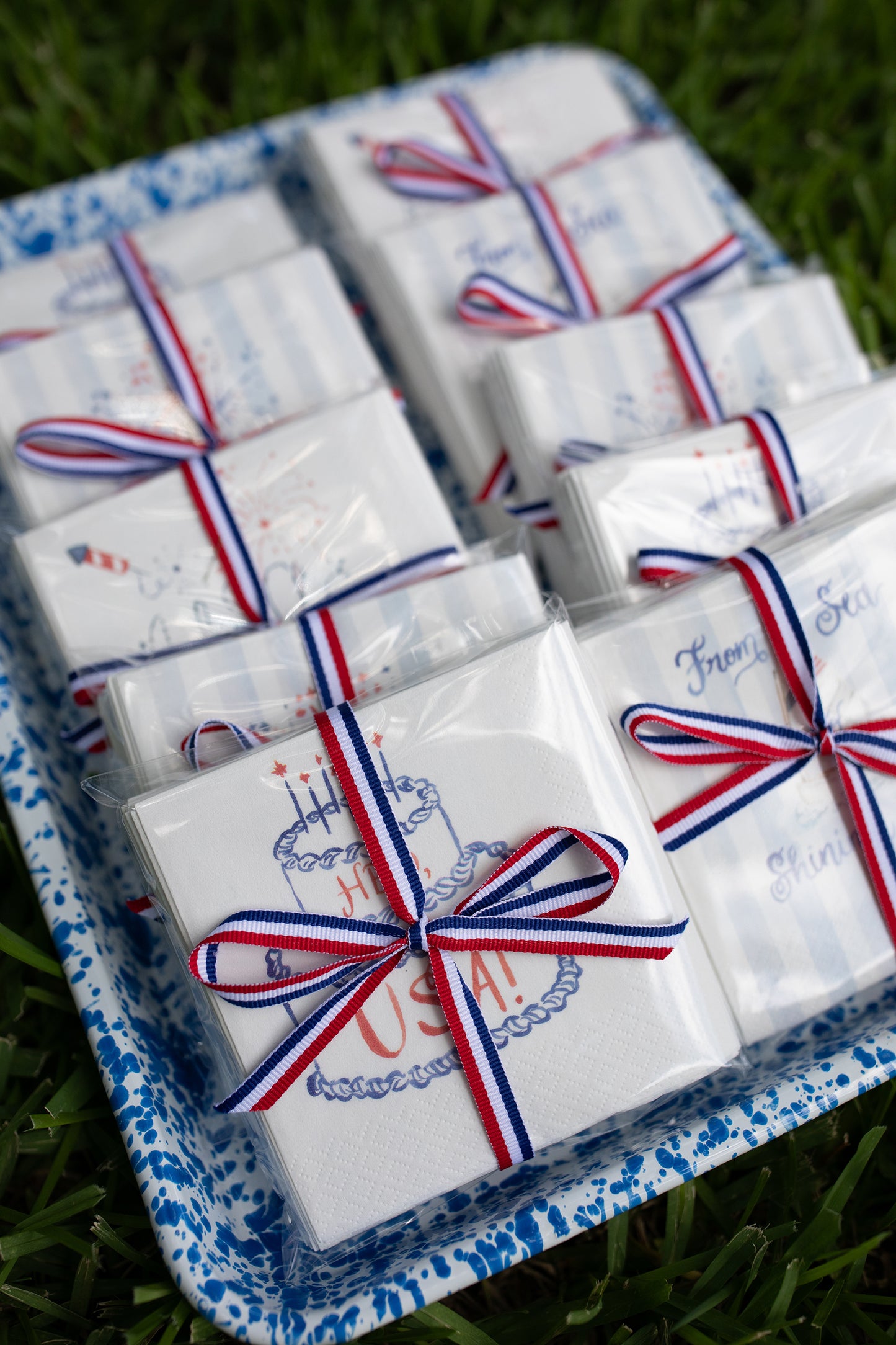 Small white boxes with red, white, and blue ribbons on a tray outdoors.