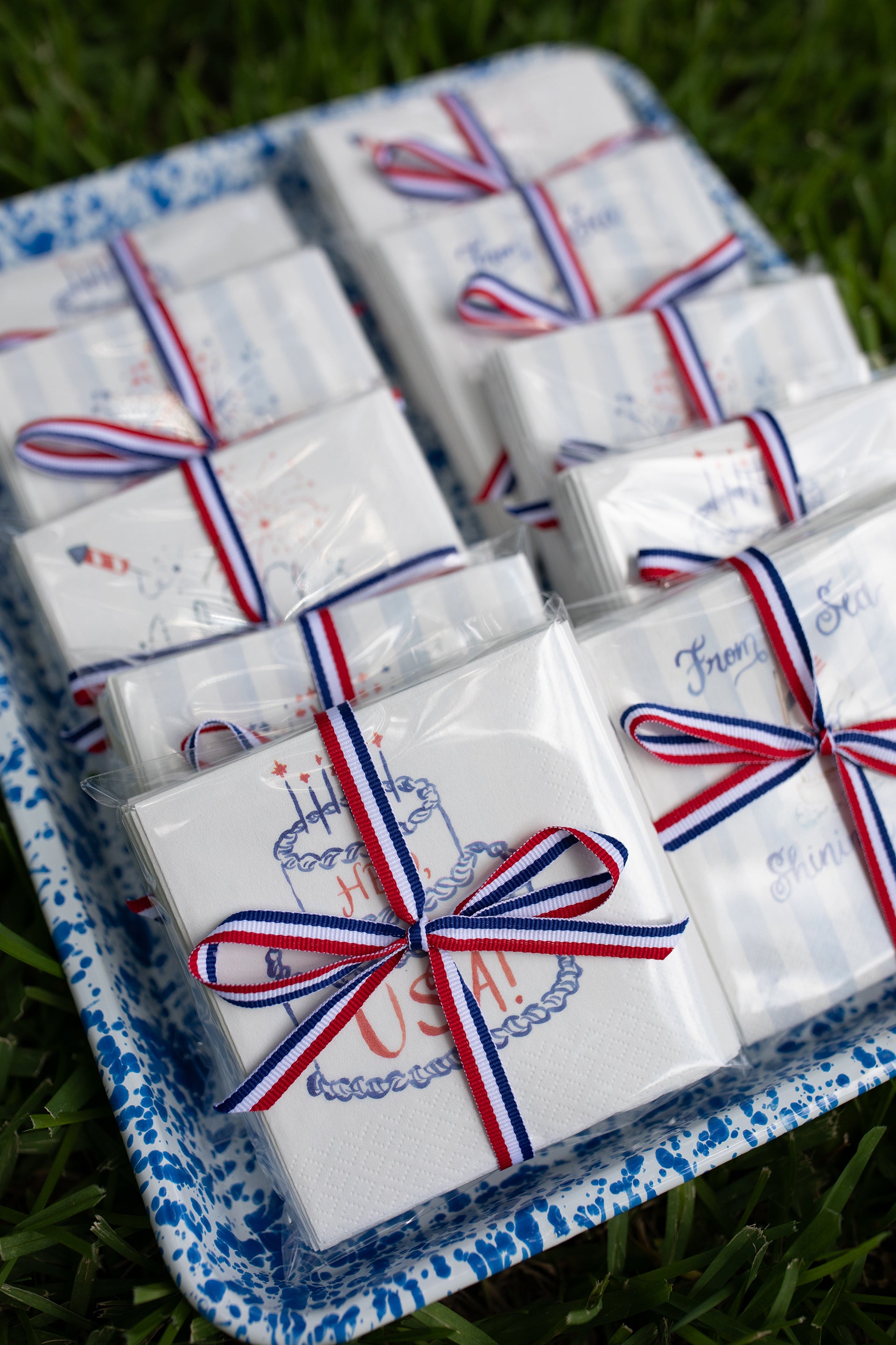 Small white boxes with red, white, and blue ribbons on a tray outdoors.